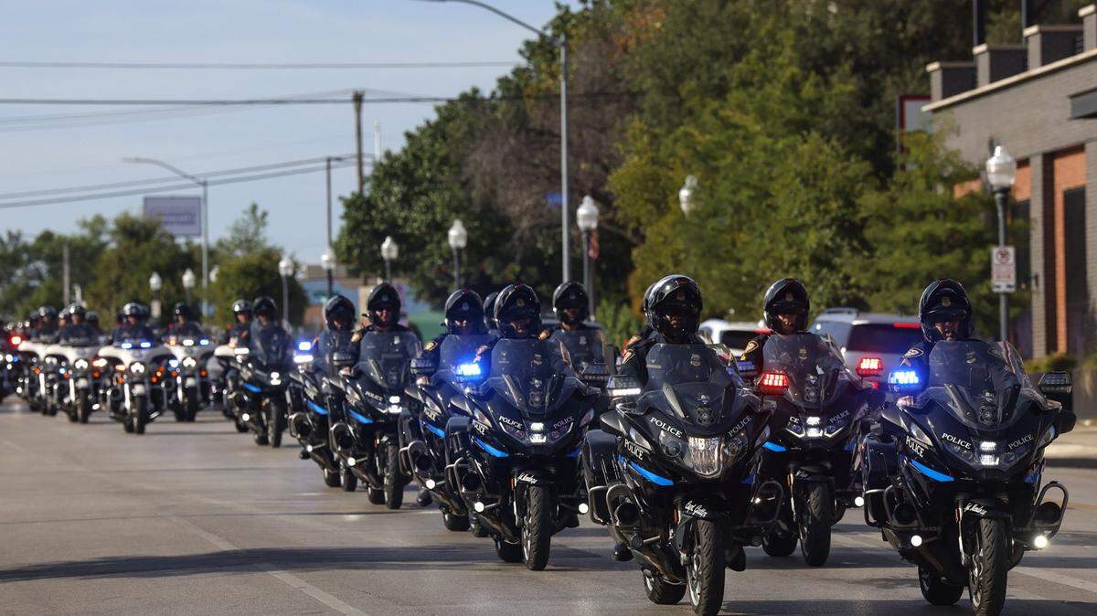 A procession of police motorcycles travels down a city street