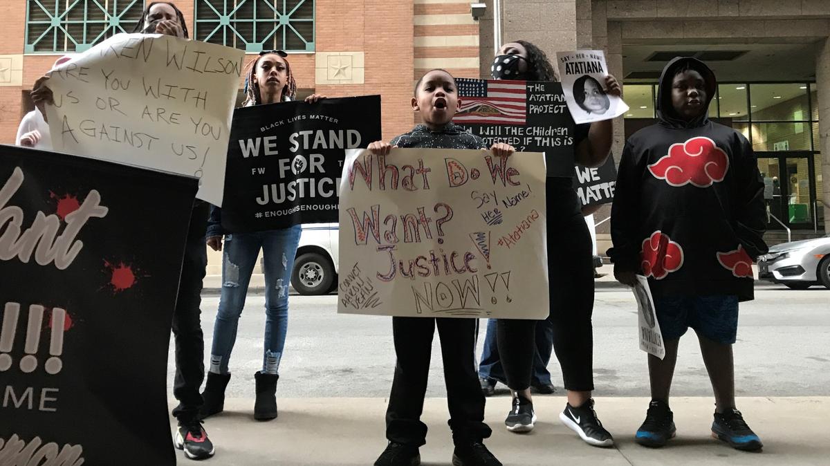 Nine-year-old Zion Carr (middle) holds up a sign on Tuesday morning in front of his aunt, Cerese Fortson (back middle right) and cousin Daleon Fortson (back right). They joined a couple dozen people at the District Attorney’s Office in downtown Fort Worth to call for a date in the trial of the officer who shot and killed Atatiana Jefferson.