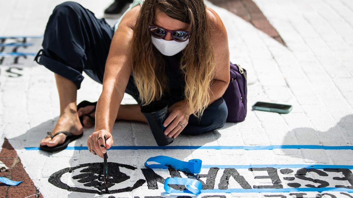 A participant paints a Black Lives Matter symbol onto the words END RACISM NOW painted along Main Street Saturday, June 27, 2020, in downtown Fort Worth.