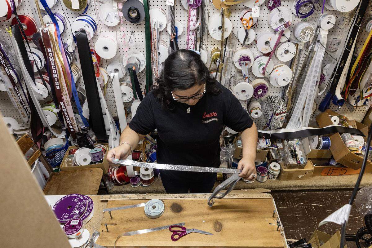 oanna Salazar stretches a length of ribbon out while in a workshop with numerous spools of ribbon behind her.