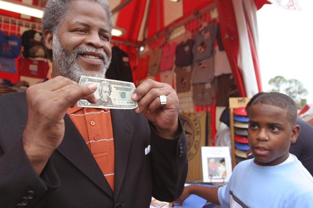 Oct. 9, 2003: Earl Campbell, former University of Texas running back No. 20, shows off a newly redesigned $20 bill for the media and others as Trey Morse, right, waits to get Campbell’s autograph. Earlier, Campbell had taken a fresh $20 from Trey Morse’s dad, William C. Morse Jr., vice president of the Federal Reserve Bank of Dallas. Campbell had taken the honor of making the first transaction in Dallas with newly redesigned bill at the Texas State Fair souvenir stand. After the event, the bills were put in circulation at the fair.