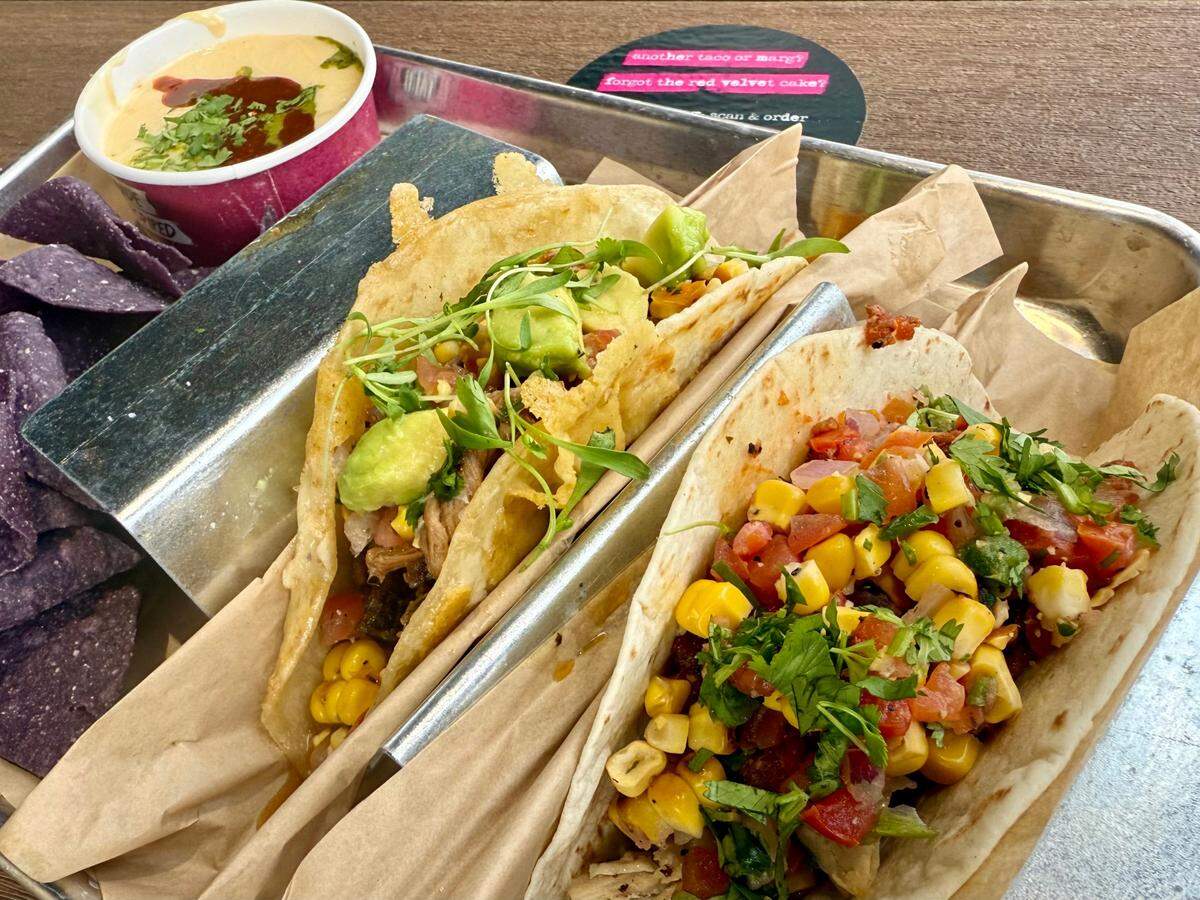 Velvet Taco’s combo platter includes two tacos — here, pollo asado on corn and brisket on a cheesy flour tortilla — with chips and white queso, guacamole, street corn or another side, seen April 26, 2025.