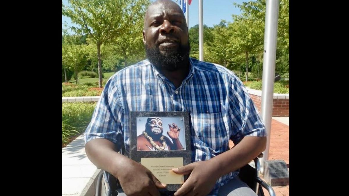 The late World Wrestling Entertainment star James Harris poses with a photo of himself in 1980s costume as “Kamala, the Ugandan Giant.” He was one of the sport’s top villains and knew fan and participant Donald Trump.