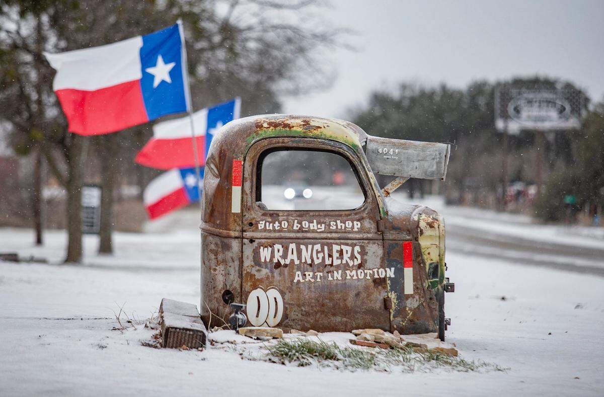 A car makes it way down a snowy Acton Highway in Hood County as the wind whipped up flags on the roadside.