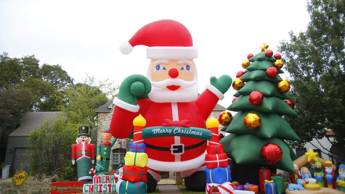 A 40-foot inflatable Santa and Christmas Tree are in front of a house. The yard is also decorated with inflatable nutcracker, elf, and nativity scene.