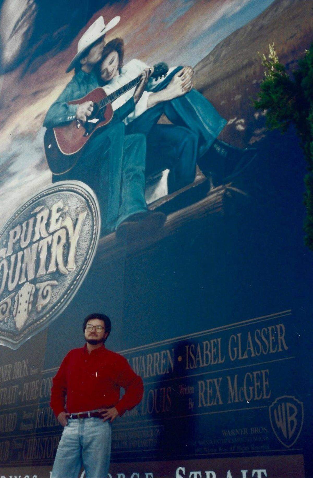 “Pure Country” screenwriter and North Texas native Rex McGee stands below a billboard of his movie.