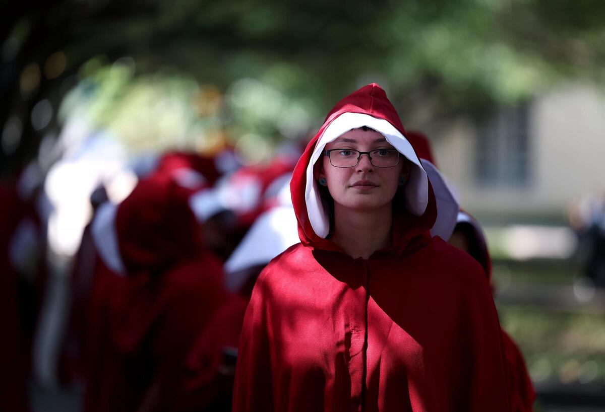 A protesters dressed in Handmaids costume prepares to march with others at Burnett Park for Indivisible 12’s March of Dissent on June 14, 2025.