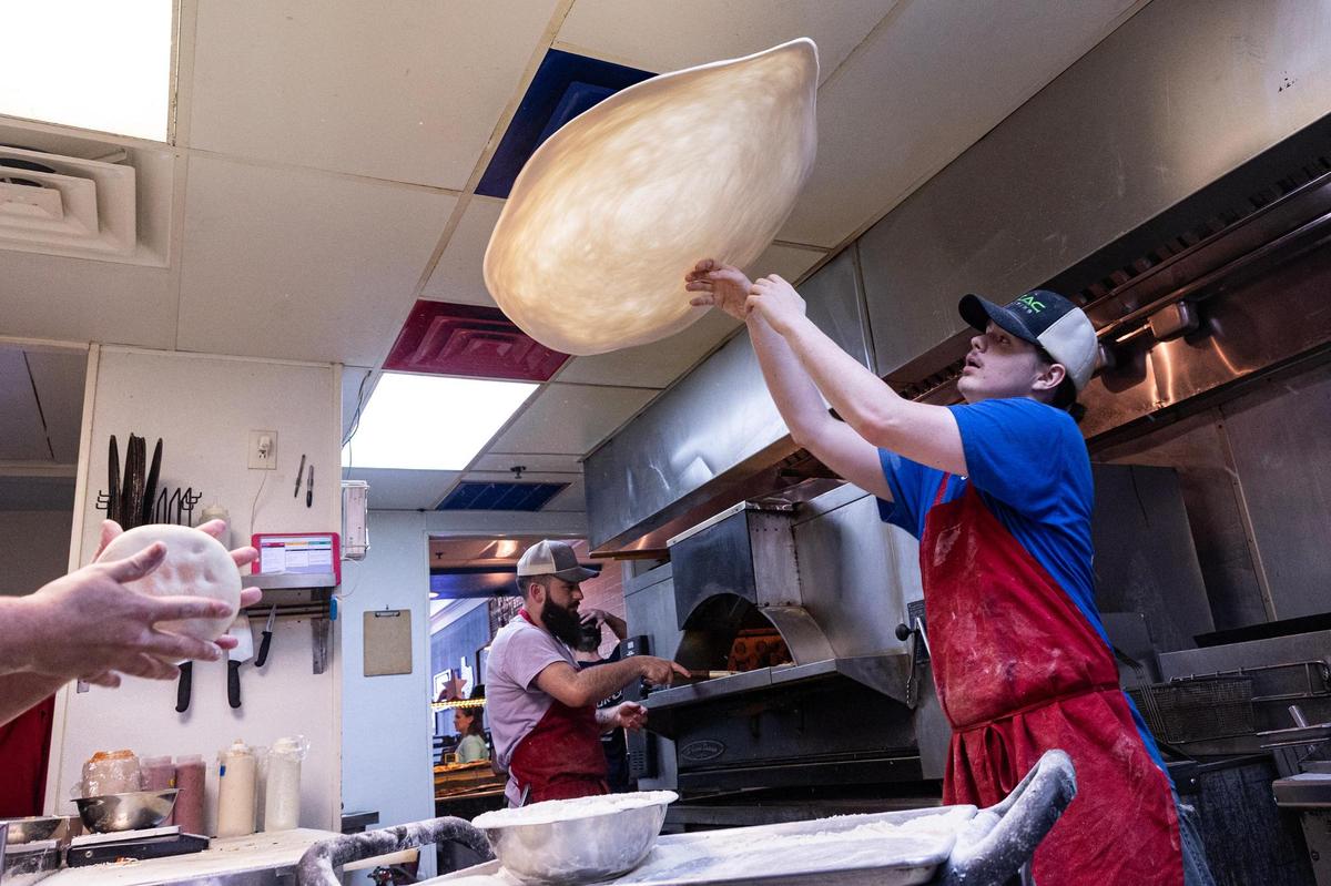 Pizza maker Kolby Hamblin, right, tosses pizza dough in the air while prep cook Raul Bautista, left, dresses the pizza during lunch service at State Street Pizza Company in Decatur on Saturday, March 29, 2025.