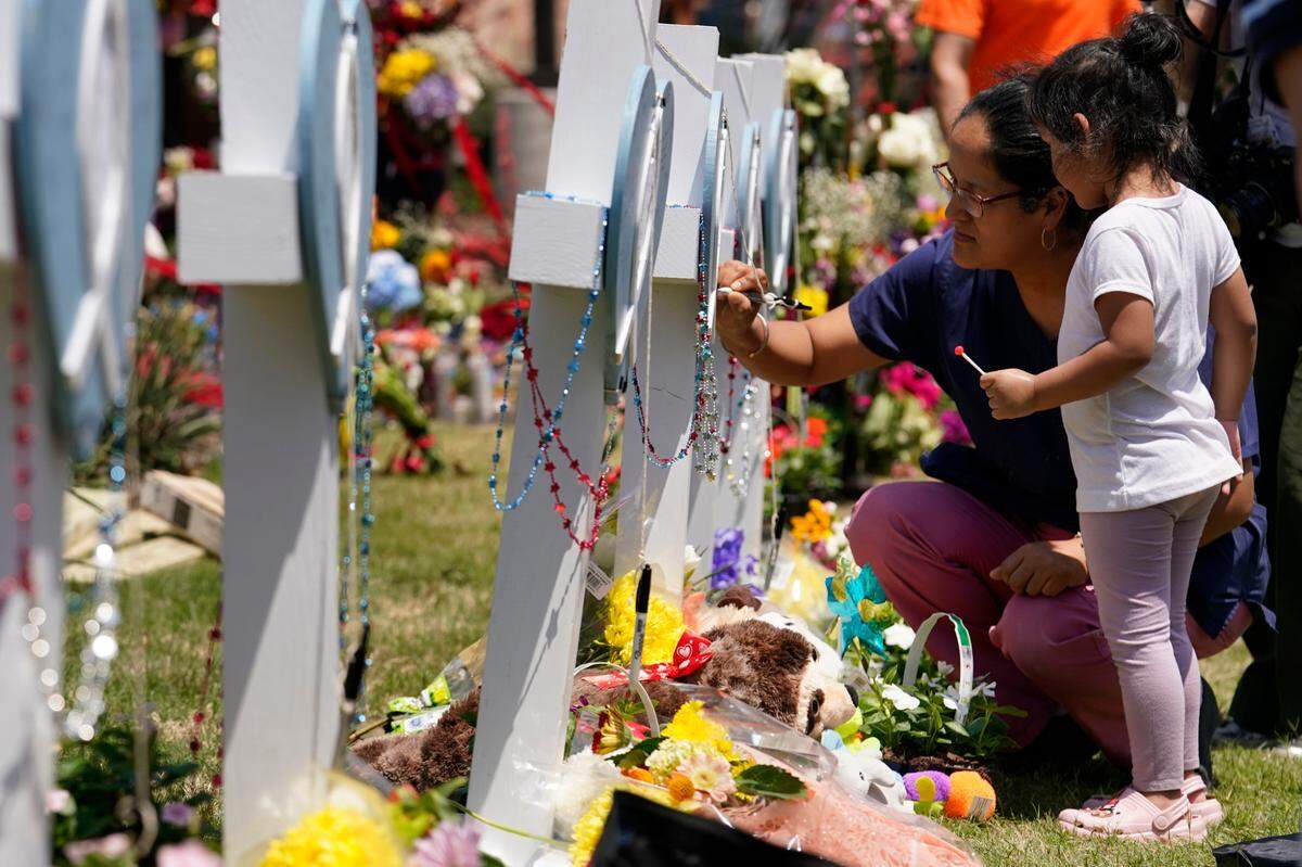 A woman signs a cross as a child looks on at a makeshift memorial by the mall where several people were killed in the May 6 mass shooting, on Monday, May 8, 2023, in Allen, Texas. (AP Photo/Tony Gutierrez)