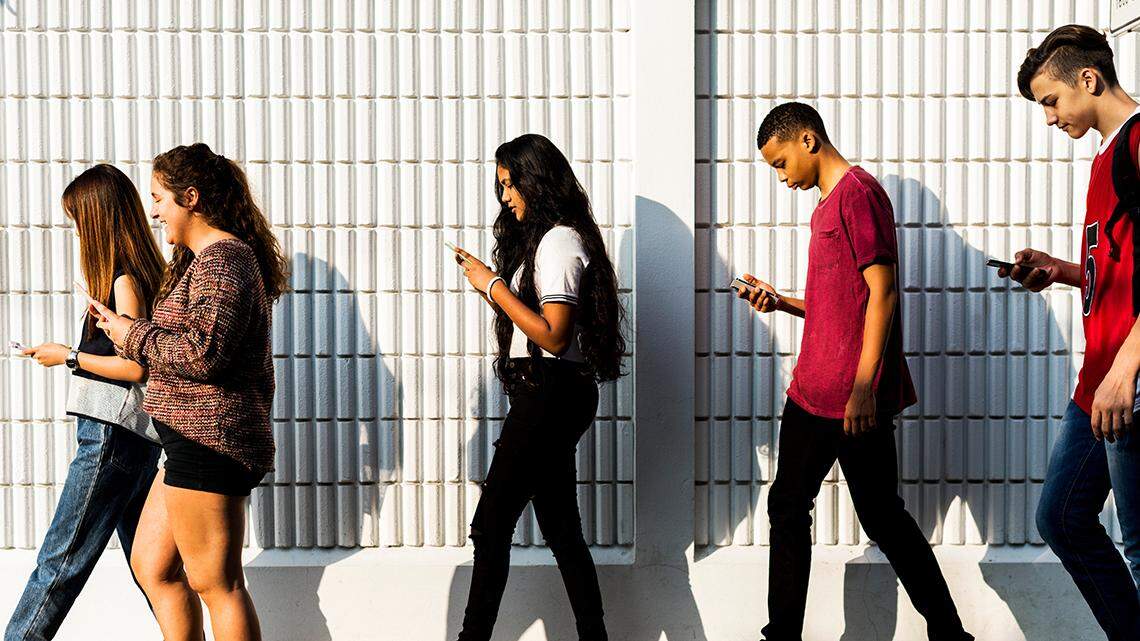 Group of young teenager friends walking home after school using smartphones addiction concept