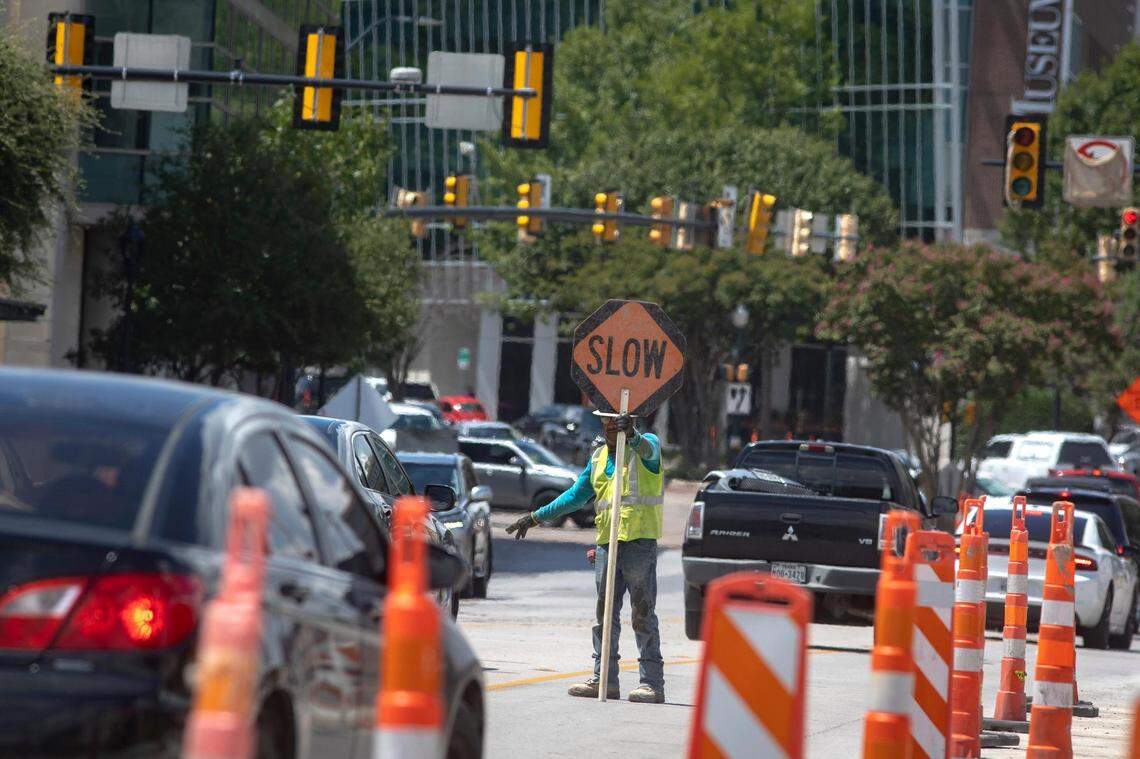 A construction worker slows drivers before a steam roller enters the roadway on West 7th Street in Fort Worth, Texas, on Friday, August 26, 2022. The construction is the city’s improvement project to make the popular corridor more pedestrian-friendly and includes new bike lanes.