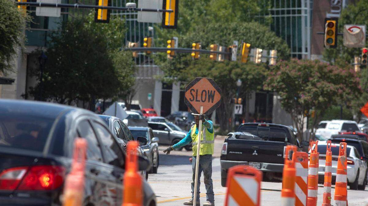 A construction worker slows drivers before a steam roller enters the roadway on West 7th Street in Fort Worth, Texas, on Friday, August 26, 2022.