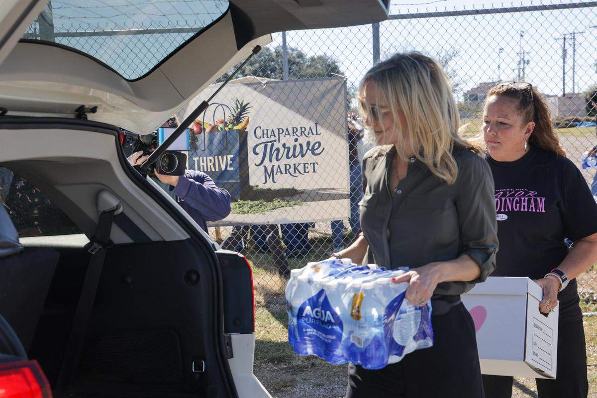 Two women load boxes into the back of an SUV. Behind them is a sign reading Chapparal Thrive Market.