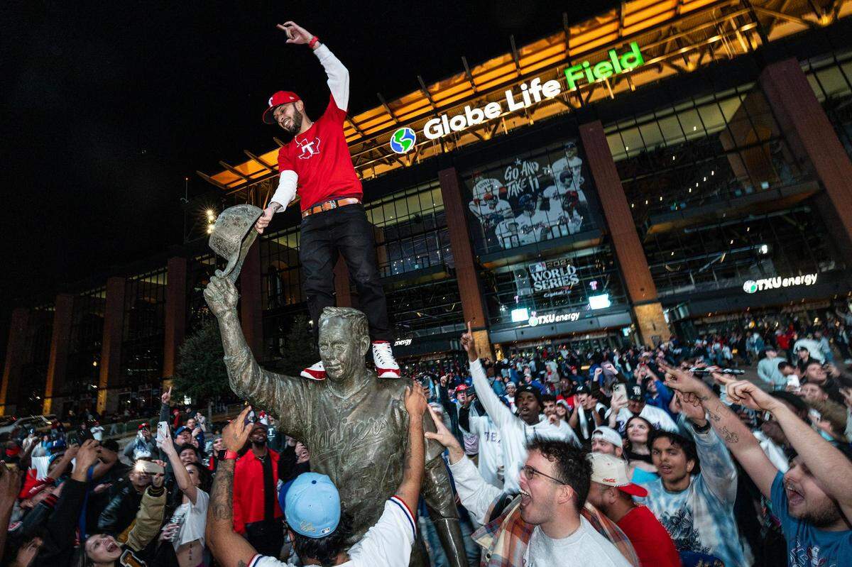 A fan climbs the Nolan Ryan Statue after the Rangers won their first World Series outside of Globe Life Field in Arlington on Wednesday, Nov.1, 2023.