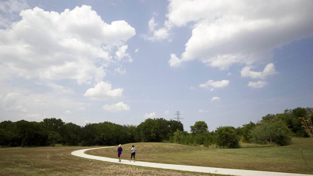 Two women jog through a city park on a sunny day.