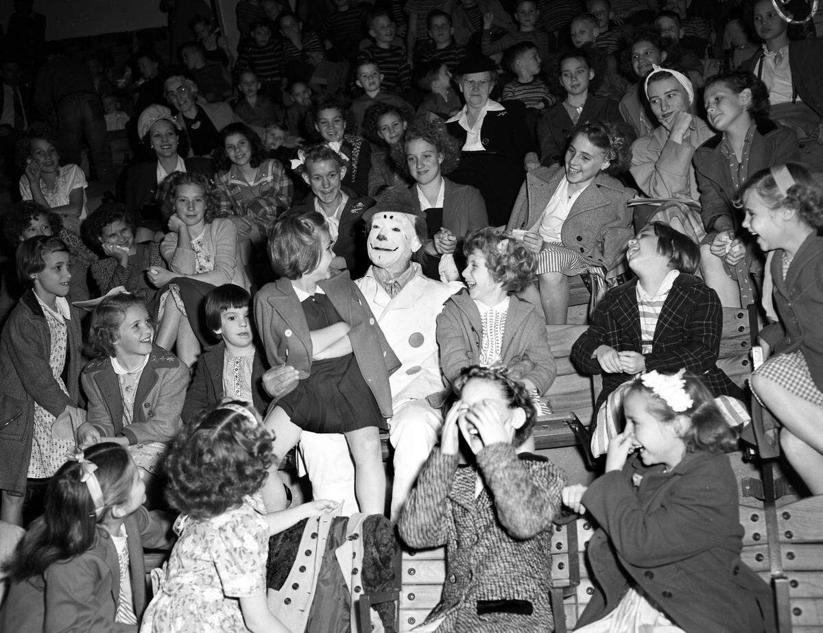  A clown is shown in the middle of seventy-nine children, one on his knee. 