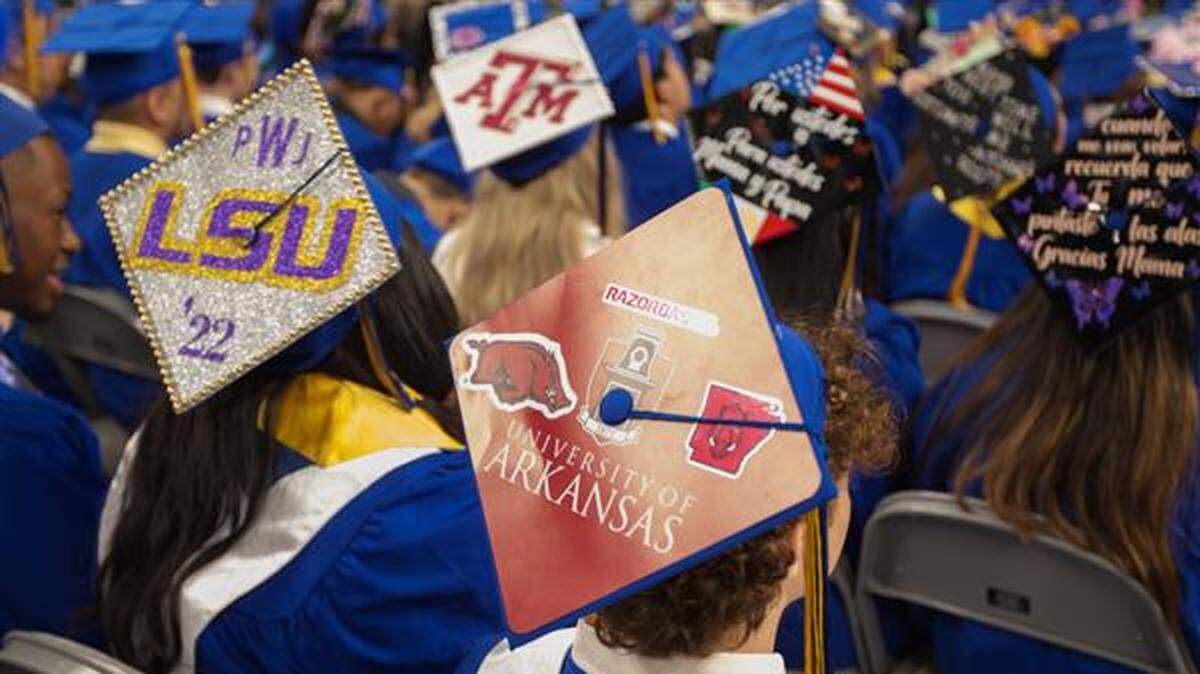 Students at Arlington Heights High School's 2022 graduation ceremony wear mortarboards bearing the logos of Louisiana State University, the University of Arkansas and Texas A&M University.