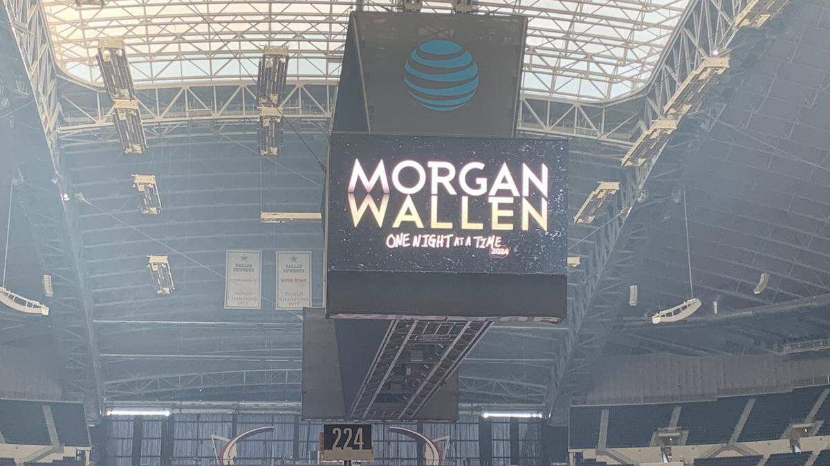 A jumbotron screen above the football field at AT&T Stadium. The words on it read, quote, Morgan Wallen One Night At A Time Tour.