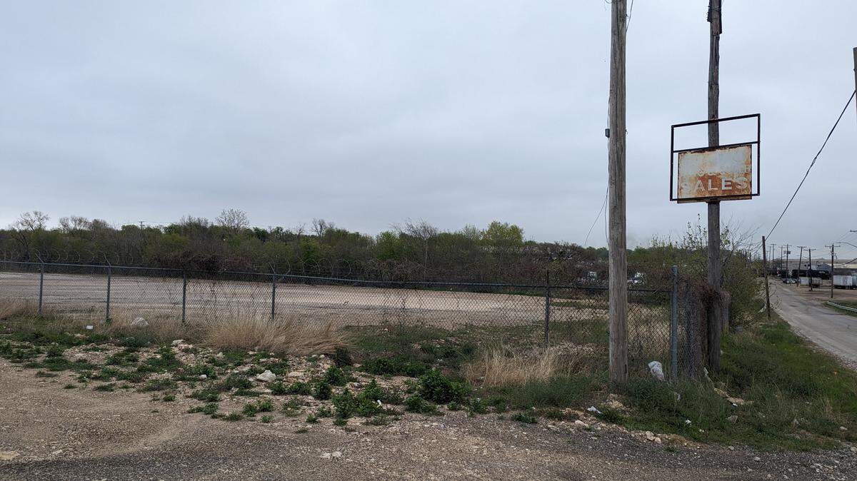 An empty lot on an overcast day with overgrown shrubs and a faded sign on the right.