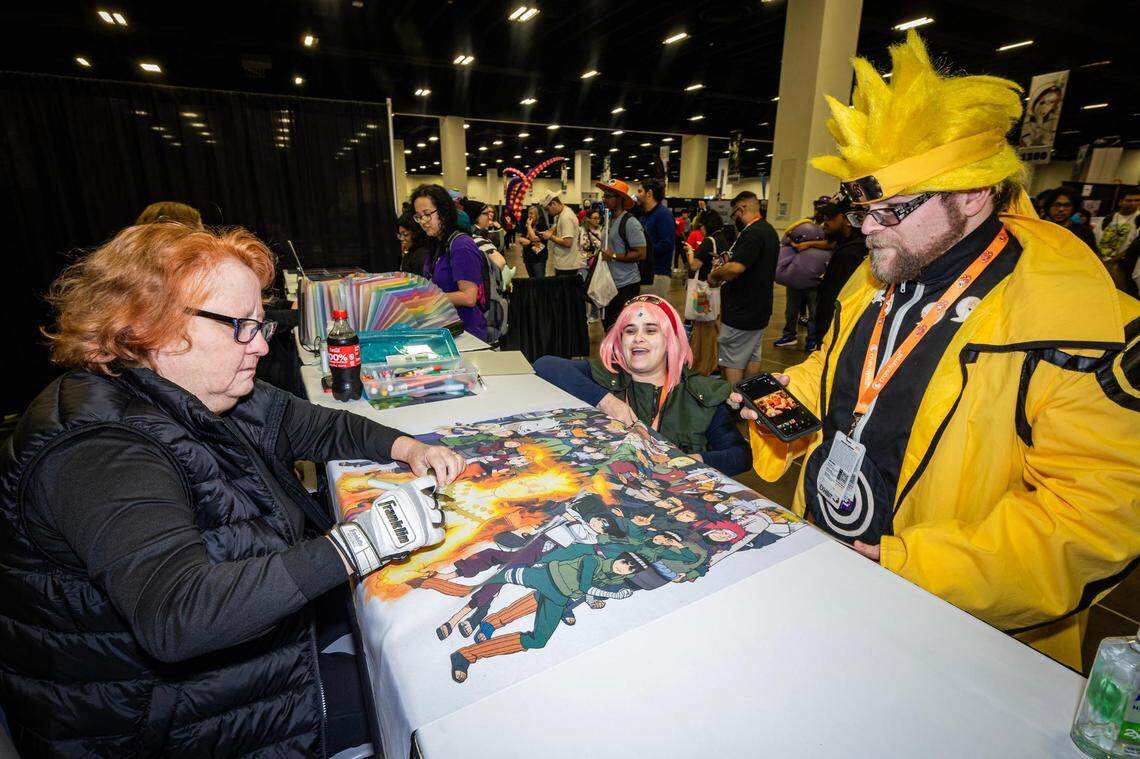 Maile Flanagan, who is the voice of Naruto Uzumaki in the English dub of “Naruto,” signs autographs for couple Ashley and Michael Ennisduring the Anime Frontier event at the Fort Worth Convention Center on Friday, Dec. 8, 2023.