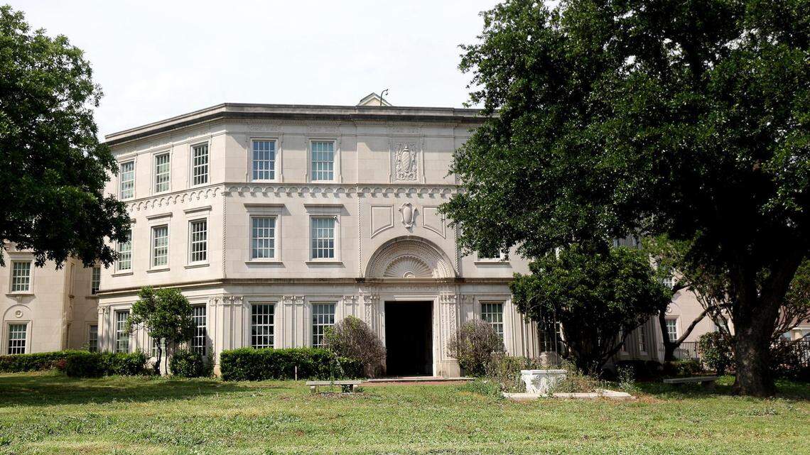 A three-story white brick building with ornate moulding, framed by two large trees.