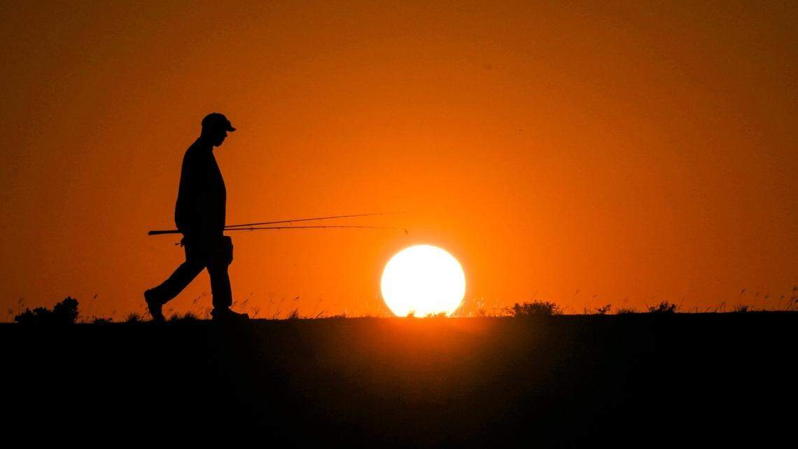 Nathaniel Robertson walks back to his car after fishing and braving the triple-digit warmth as the sun sets over Lake Pflugerville, Texas, on June 26, 2023.