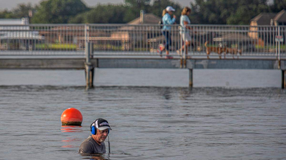 Don Mackenzie, of Grand Prairie, takes a dip in the cool water of Granbury City Beach Park with a metal detector as dog walkers cross the metal bridge over Lake Granbury, Texas, Saturday, Sept. 5, 2020