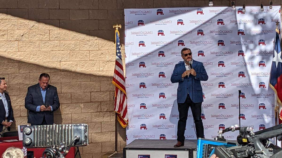Ted Cruz standing on a stage with a Tarrant County GOP sign behind him, and Republican officials just off to the left. 