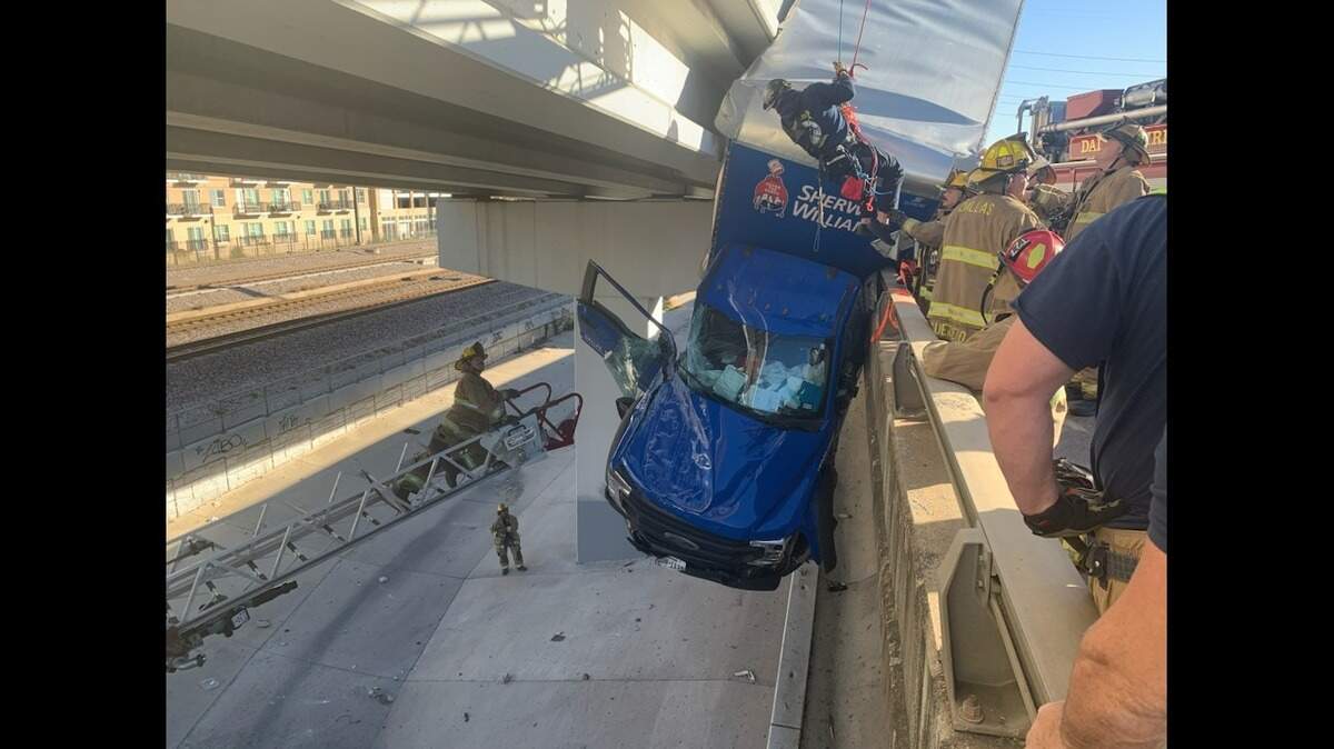 First responders work to rescue a driver in a Sherwin-Williams truck hanging off a bridge on northbound Interstate 35 near Victory Avenue in Dallas County on Monday afternoon.