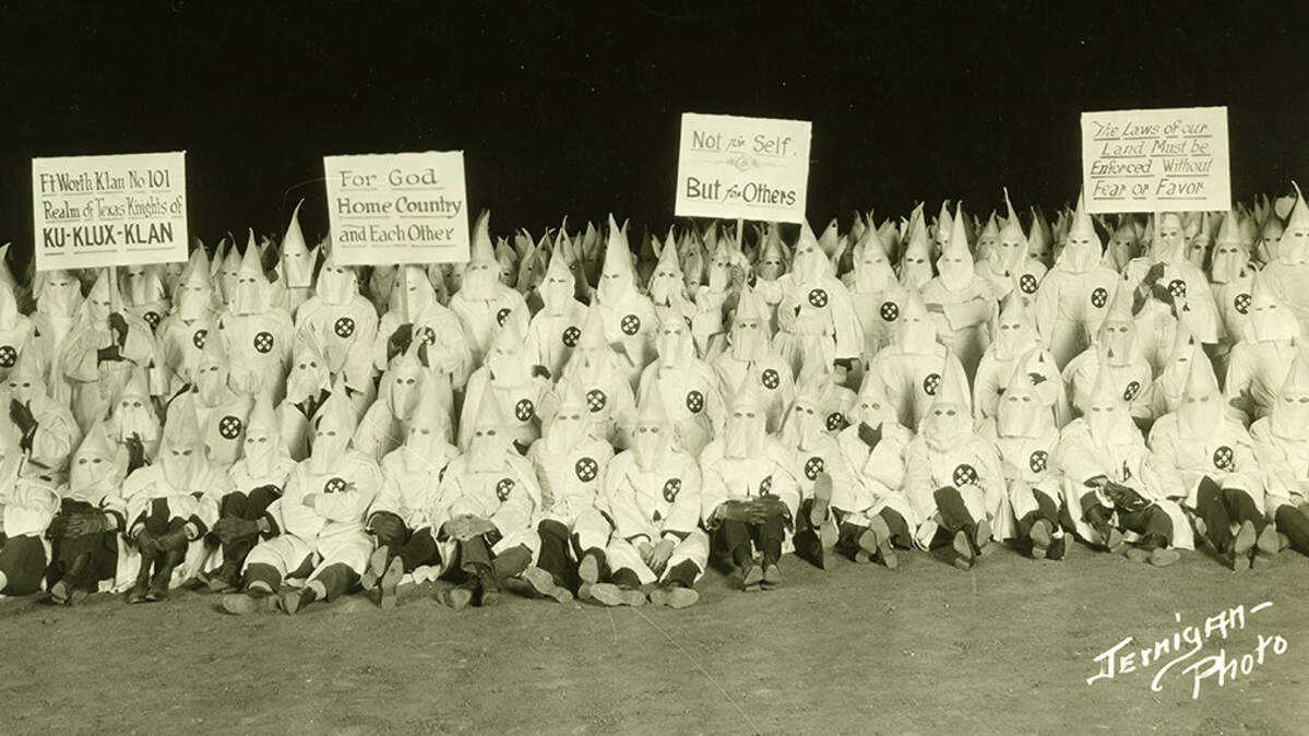 Ku Klux Klan gathering of the Fort Worth Klan No. 101; Klan members in robes and hoods holding signs, no date [ca. early 1920s] Photographer: Jernigan
