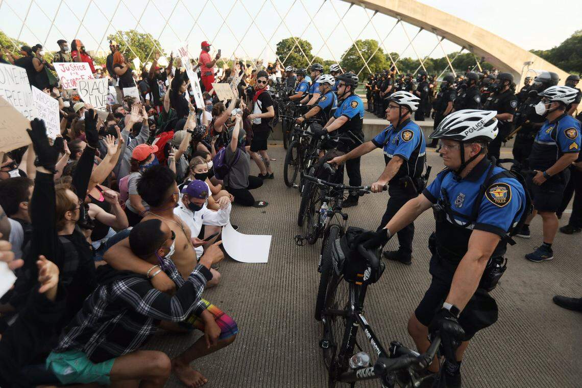 Fort Worth protesters locked arms and then knelt as they approached a line of officers, some of whom were wearing riot gear and gas masks, blocking the other side of a bridge over the Trinity River. Marchers were trying to get to the West 7th District.