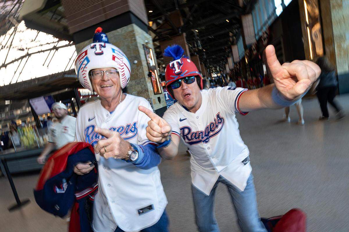 Father and son Galen and Christopher Killion cheer as they enter the stadium with their custom made Texas Rangers helmets for the 2024 season opener between the Rangers and the Chicago Cubs at Globe Life Field in Arlington on Thursday, March 28, 2024.