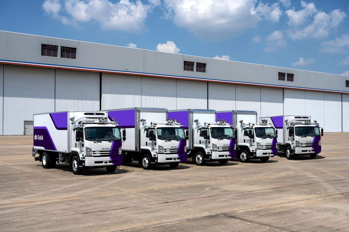 Five Gatik self-driving trucks are parked next to each other in a row. The box trucks range in size from 20 feet to 26 feet.