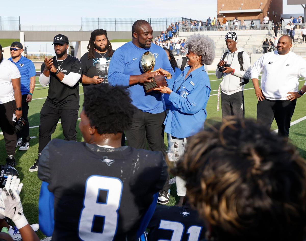 Crowley school board member June Davis presents North Crowley head coach Ray Gates with the trophy after a UIL Class 6A D1 Bi-district playoff football game at Crowley ISD Multi-Purpose Stadium in Fort Worth, Texas, Saturday, Nov. 16, 2024.