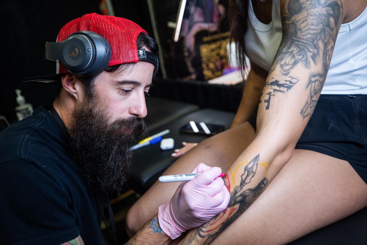 Granbury resident Cody Anderson, left, draws an outline of a tattoo for Granbury resident Alyssa Hill during Fort Worth Tattoo Arts Festival on Friday, June 7, 2024, at the Fort Worth Convention Center. Anderson is adding filler to a previously drawn tattoo.