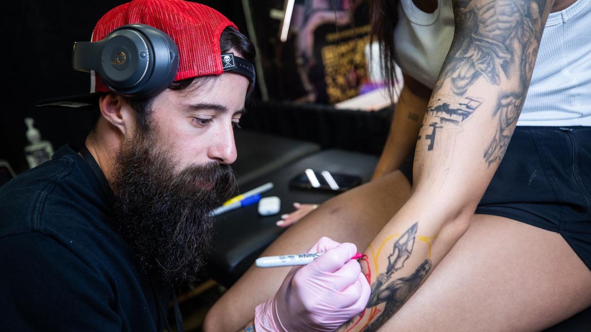 Granbury resident Cody Anderson, left, draws an outline of a tattoo for Granbury resident Alyssa Hill during Fort Worth Tattoo Arts Festival on Friday, June 7, 2024, at the Fort Worth Convention Center. Anderson is adding filler to a previously drawn tattoo.