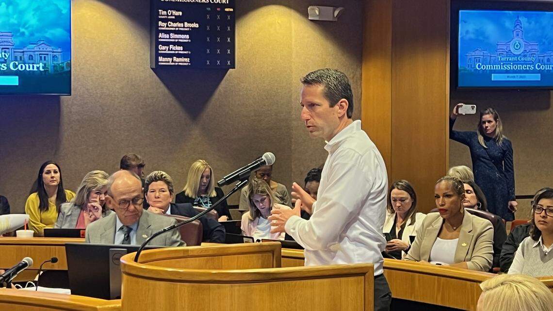 A man in a white dress shirt stands in front of a crowd to speak at the Tarrant County Commissioners meeting. 