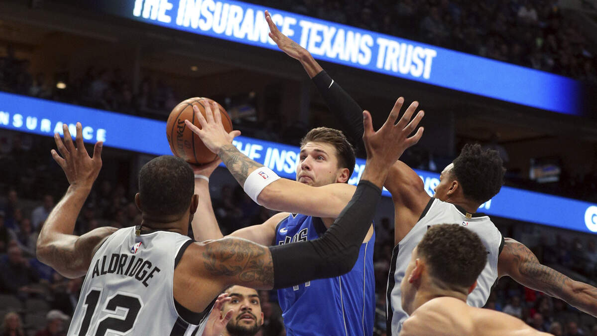Dallas Mavericks forward Luka Doncic (77) puts up a shot against San Antonio Spurs center LaMarcus Aldridge (12) and San Antonio Spurs guard Dejounte Murray (5) in the first half of an NBA basketball game Monday, Nov. 18, 2019, in Dallas. (AP Photo/Richard W. Rodriguez)