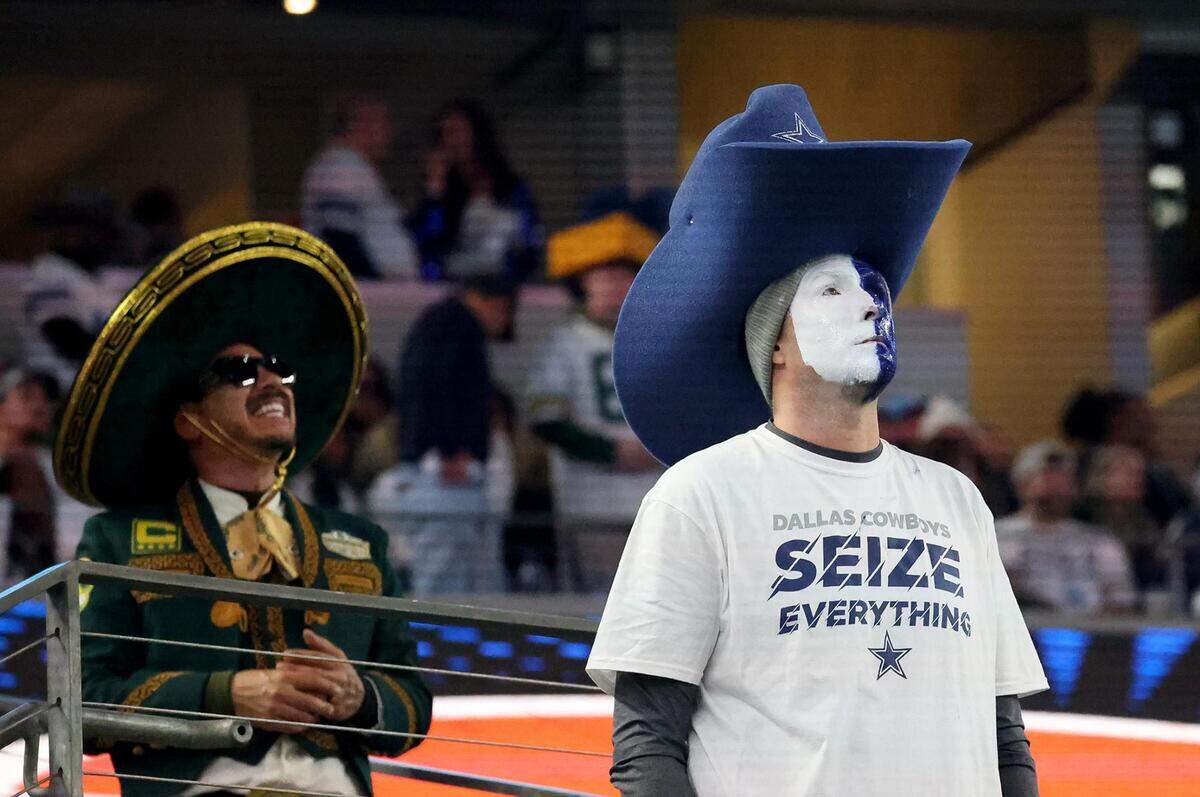 A Dallas Cowboys fan looks solemn as a Green Bay Packers fan smiles behind him during the third quarter of the NFC wild-card playoff game on Sunday, January 14, 2024, at AT&T Stadium in Arlington. The Dallas Cowboys were defeated 48-32.
