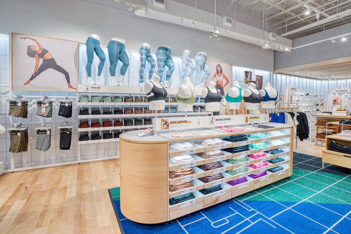 The Nike store features a table with stacks of multi-colored women's sports bras of varying styles. Behind the table is a wall with mannequins sporting different styles of leggings above stacks of different styles and sizes.