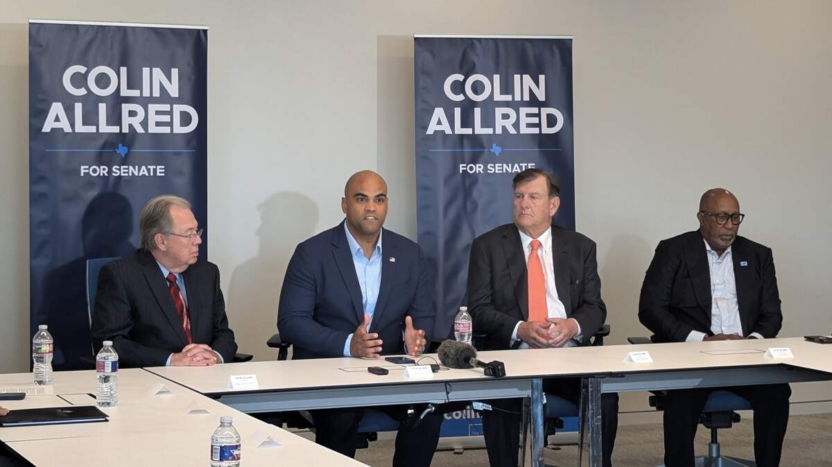 Four men sitting behind a table with signs for Senate Candidate Colin Allred in the background