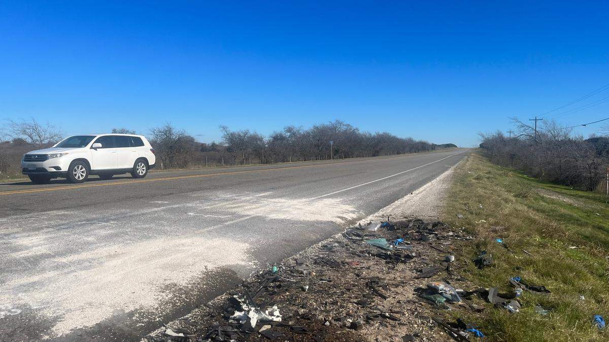 Debris sits on the right side of a roadway as a white car travels past in the opposite lane.