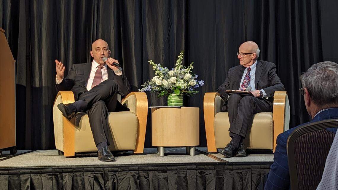 Two guys sitting in chairs on a stage talking to an audience. 