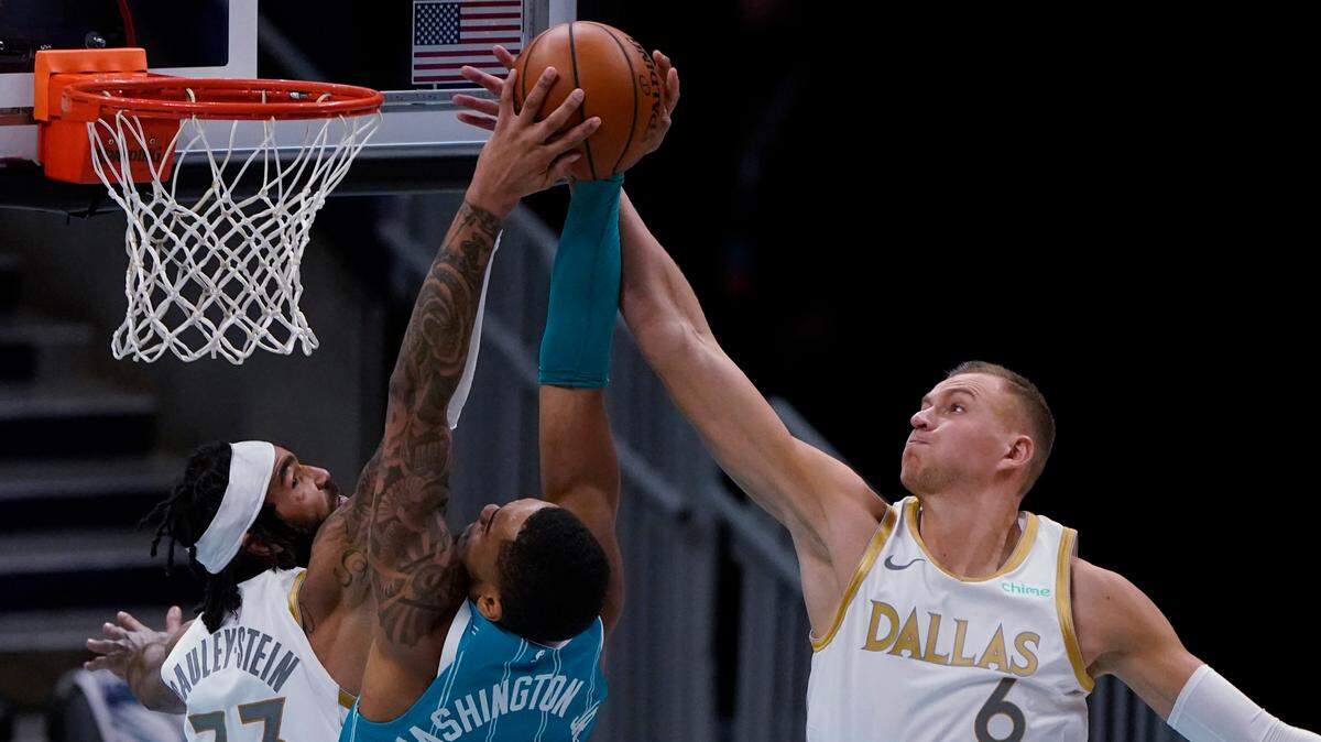 Dallas Mavericks’ Kristaps Porzingis, right, blocks a shot by Charlotte Hornets forward P.J. Washington as center Willie Cauley-Stein defends during the second half of Wednesday’s game. Porzingis finished with 21 points in his season debut.