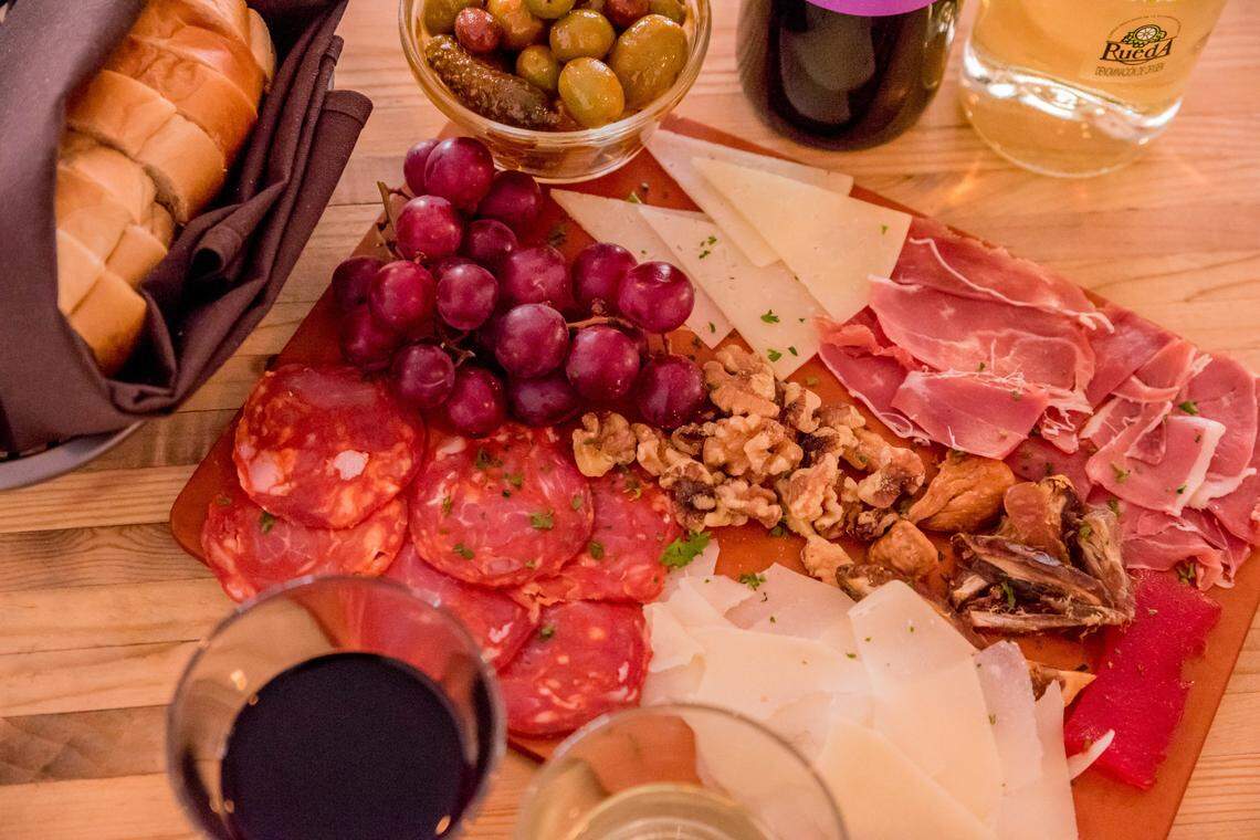 A board with ham, cheese, nuts and fruit and bread on the side.