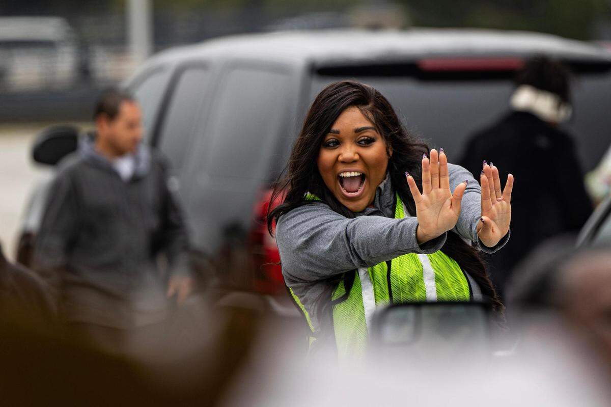 Aisha Schutz signals for a car to stop while volunteering put groceries in their trunk for the 4th annual Thanksgiving Mobile food distribution at AT&T Stadium in Arlington on Friday, November 17, 2023.