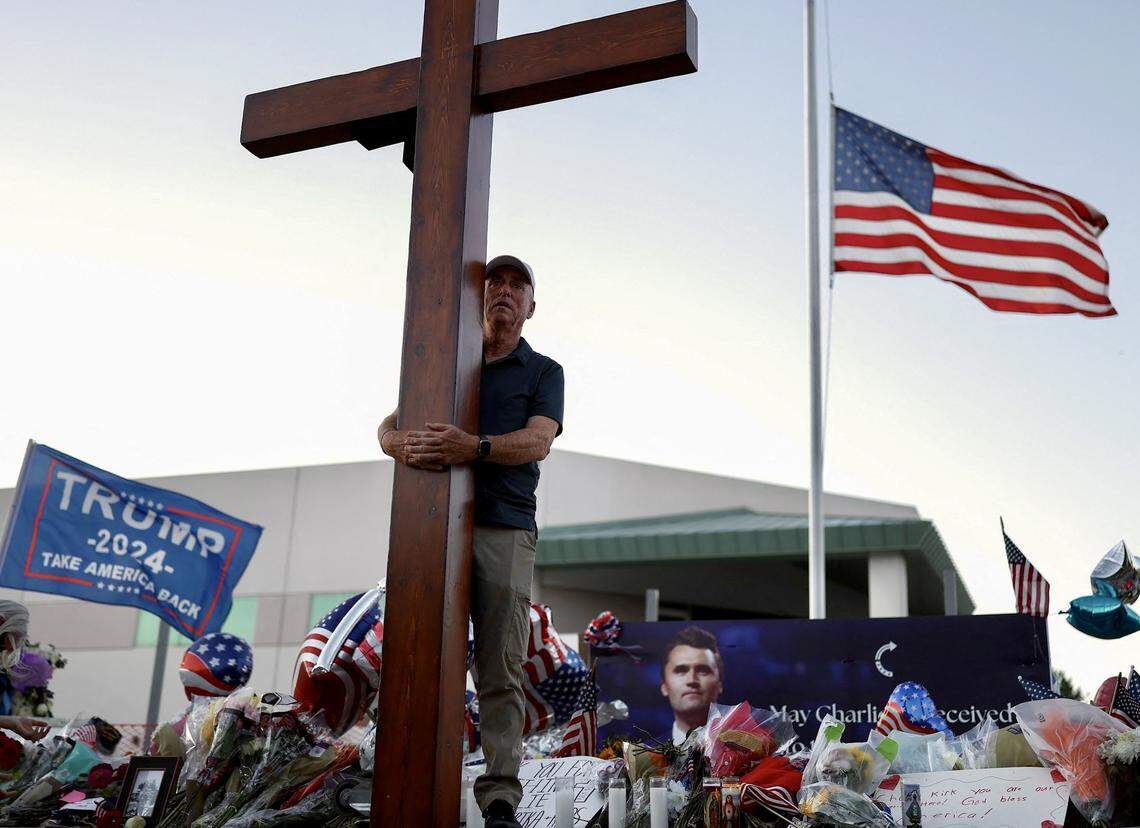 A U.S. flag flies at half-staff as a man carries a large cross near a makeshift memorial for Turning Point USA Founder Charlie Kirk outside of the Turning Point USA headquarters in Phoenix, Arizona, on Sept. 12, 2025.