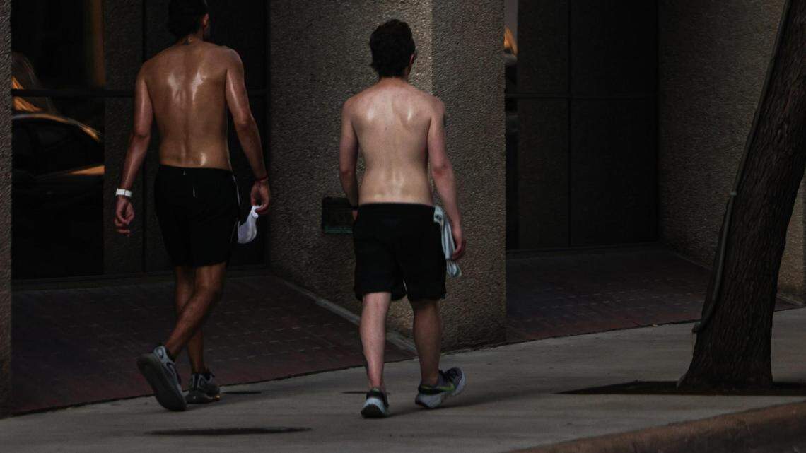 Two sweaty men walking away with their shirts off and wearing shorts.