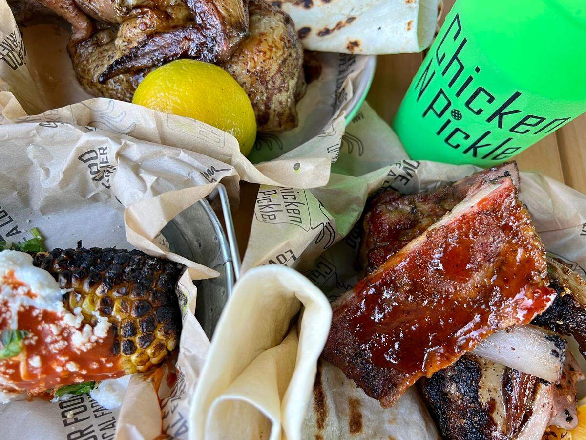 Chicken n Pickle serves wood-roasted chicken (top) seasoned four ways, plus ribs and sides such as elote (left).