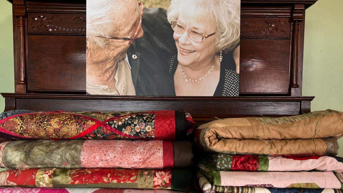 A photo of Verna Mae Brashear and Bobbie Brashear Sr. in front of her quilts.